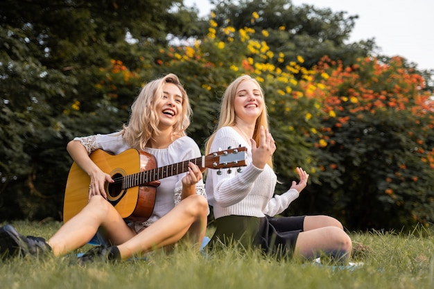Portrait de jeunes femmes de race blanche assis dans le parc en plein air et jouer de la guitare chanter une chanson avec bonheur