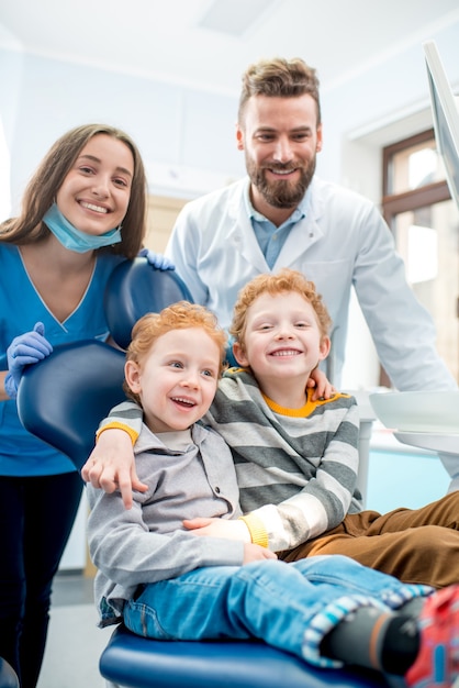 Portrait de jeunes garçons heureux assis sur la chaise avec un dentiste et une assistante au cabinet dentaire