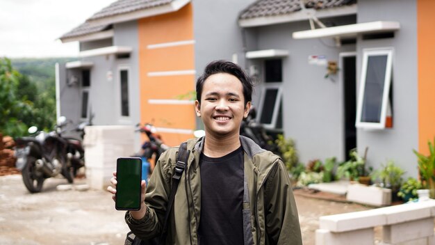 Portrait de jeunes hommes debout devant leur nouvelle maison tenant un téléphone vert