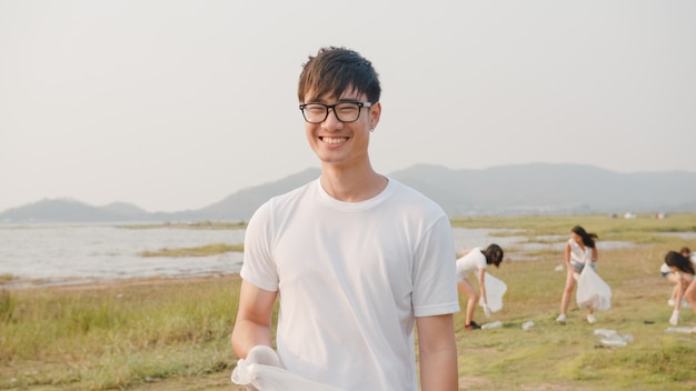 Portrait de jeunes volontaires asiatiques aident à garder la nature propre, regardant devant et souriant avec des sacs poubelles blancs sur la plage