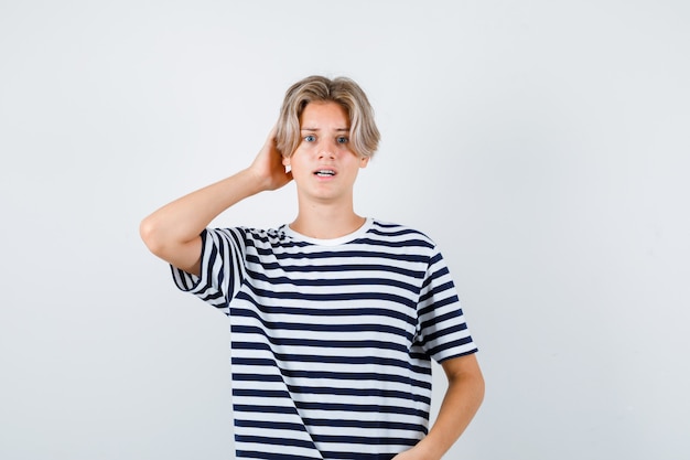 Portrait d'un joli garçon adolescent avec la main derrière la tête en t-shirt rayé et à la vue de face confuse