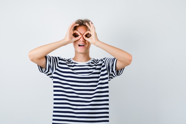 Portrait D'un Joli Garçon Adolescent Montrant Un Geste De Lunettes En T-shirt Rayé Et Se Demandant En Vue De Face