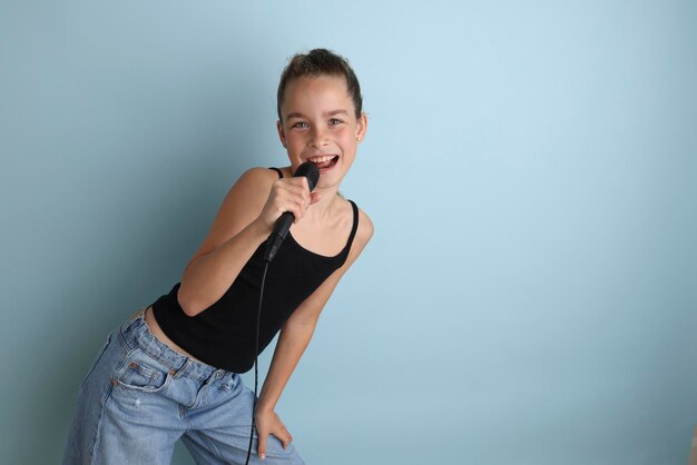 Portrait d'une jolie adolescente chantant à l'aide d'un microphone Adolescente en t-shirt noir sur un fond bleu isolé Karaoké pour enfants divertissement à domicile pour enfants