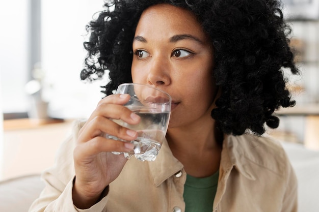 Photo portrait d'une jolie belle femme afro-américaine tenant un verre d'eau potable dans l'appartement