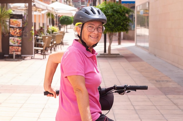 Portrait d'une jolie cycliste âgée souriante courant avec un vélo électrique dans une rue de la ville en regardant la caméra