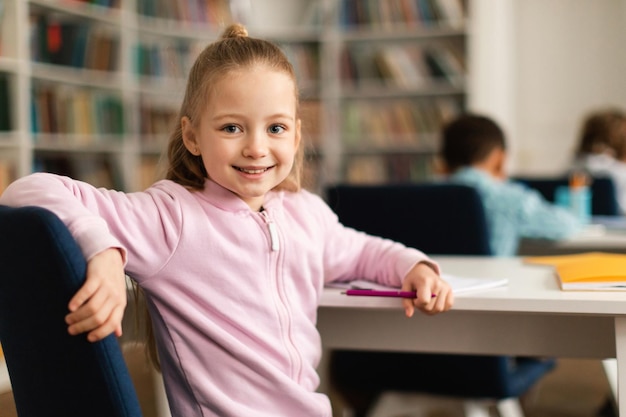 Portrait d'une jolie élève d'école assise à son bureau dans la salle de classe se retournant et souriant à