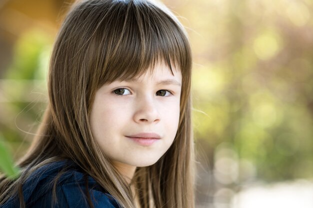 Portrait de jolie enfant fille aux yeux gris et longs cheveux blonds à l'extérieur sur fond clair flou. Mignon enfant femelle sur une chaude journée d'été à l'extérieur.