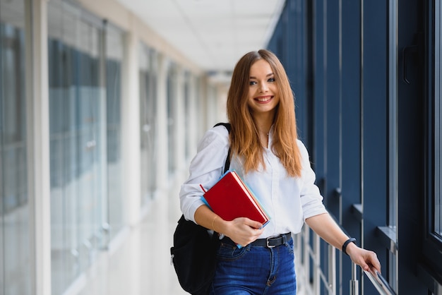 Portrait d'une jolie étudiante avec des livres et un sac à dos dans le couloir de l'université