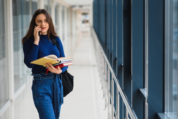 Portrait d'une jolie étudiante avec des livres et un sac à dos dans le couloir de l'université