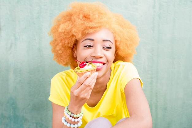 Portrait d'une jolie femme africaine en t-shirt jaune tenant un dessert sucré à la cerise sur fond vert