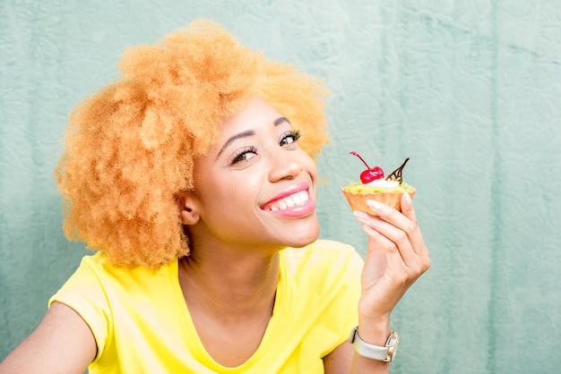 Portrait D'une Jolie Femme Africaine En T-shirt Jaune Tenant Un Dessert Sucré à La Cerise Sur Fond Vert