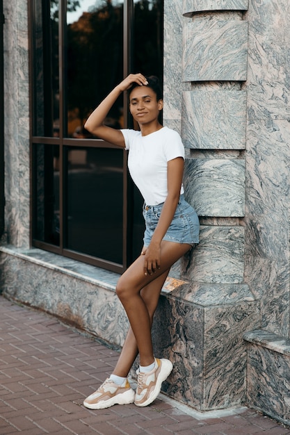 Portrait de jolie femme afro-américaine sur des shorts et des t-shorts sur mur gris