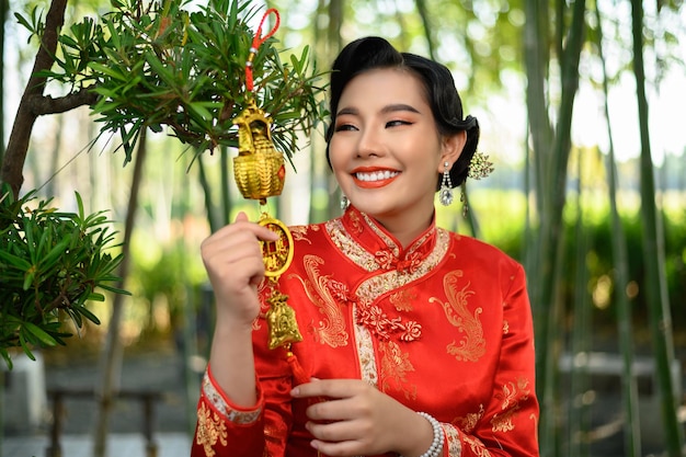 Portrait jolie femme asiatique dans un sourire cheongsam chinois et tenant une amulette dorée pour les décorations de symbole porte-bonheur du Nouvel An chinois