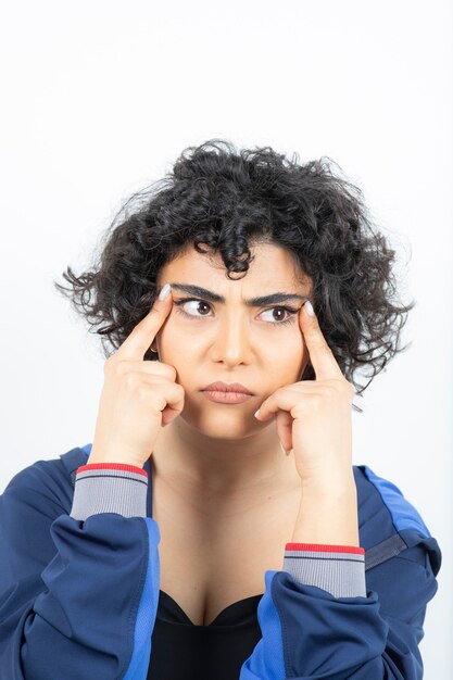 Portrait d'une jolie femme aux cheveux bouclés tenant les doigts près des sourcils.