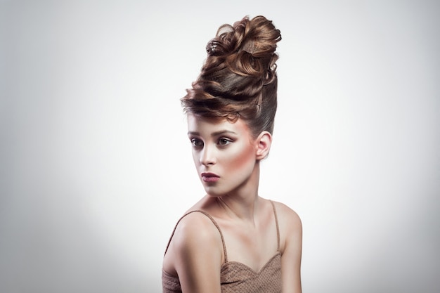 Portrait d'une jolie femme brune avec une coiffure élégante et un maquillage portant un singulet beige regardant de côté sur fond gris isolé. intérieur, tourné en studio sur l'espace de copie.