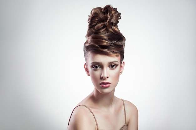 Portrait d'une jolie femme brune avec une coiffure élégante et un maquillage regardant la caméra avec un visage sérieux sur fond gris isolé. intérieur, tourné en studio sur l'espace de copie.