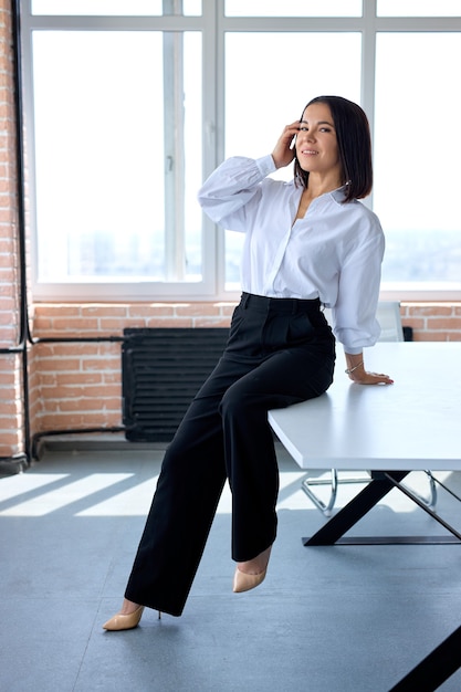 Portrait de jolie femme brune de race blanche dans des vêtements formels assis sur la table de bureau