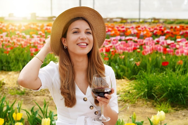 Portrait de jolie femme buvant un verre de vin rouge sur fond fleuri regardant sur le côté avec un visage heureux souriant