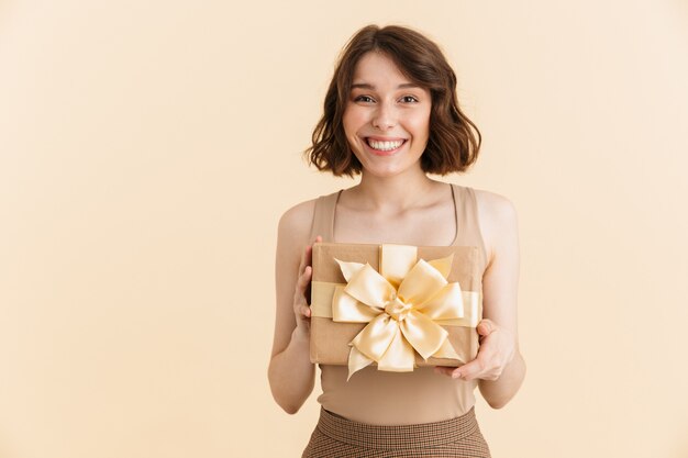 Portrait d'une jolie femme caucasienne des années 20 vêtue de vêtements décontractés souriant tout en tenant une boîte présente isolée