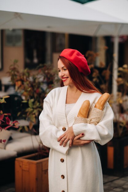 Portrait d'une jolie femme dans un béret rouge et un cardigan blanc avec des baguettes dans ses mains se promenant dans la ville d'automne