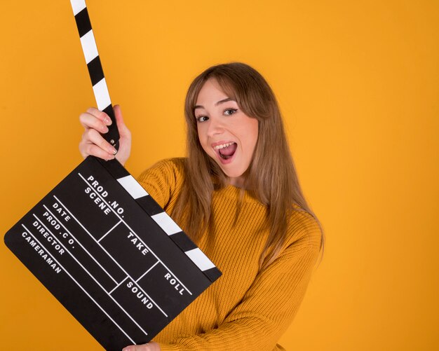 Portrait de jolie femme heureuse, souriant, avec clap, sur fond jaune-orange