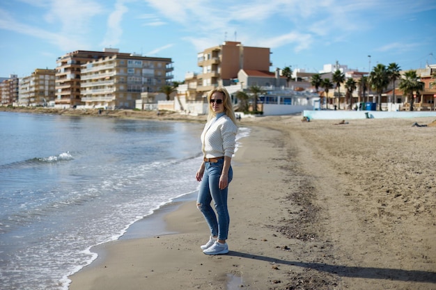 Portrait d'une jolie femme marchant le long de la plage de la ville sur fond de mer