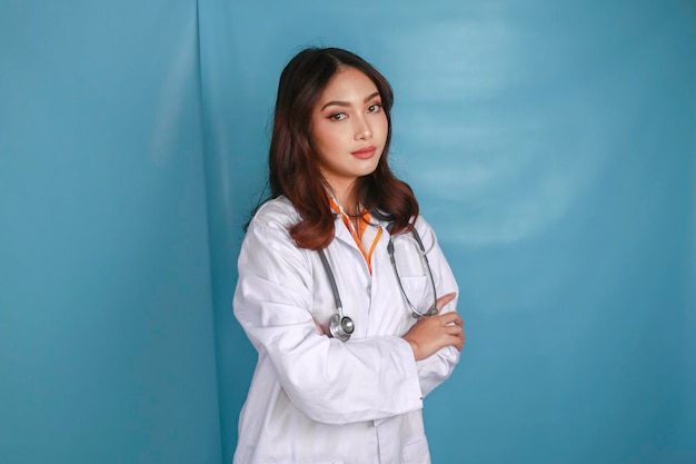 Portrait d'une jolie femme médecin souriante amicale et confiante, les bras croisés, porter un stéthoscope de laboratoire blanc isolé sur fond de couleur bleue