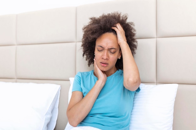 Portrait d'une jolie femme noire au lit à la maison avec un mal de tête ressentant de la douleur et avec une expression de malaise