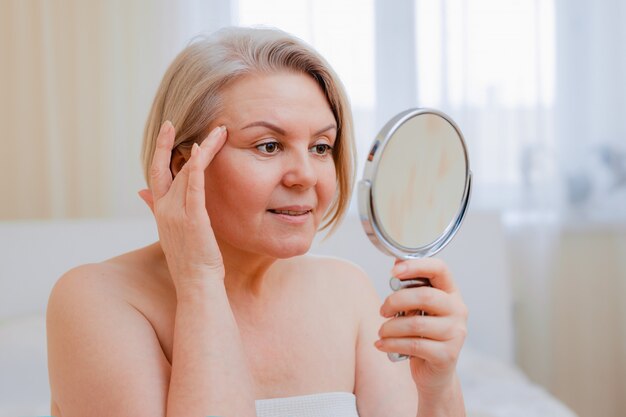 Portrait Jolie Femme Senior Avec Les Mains Sur Son Miroir De Visage à La Maison Après La Salle De Bain