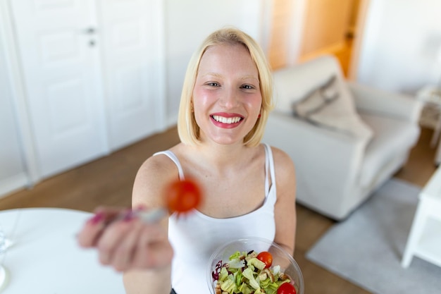 Portrait d'une jolie femme souriante caucasienne mangeant de la salade Jeune et heureuse femme mangeant une salade saine avec des ingrédients frais verts à l'intérieur