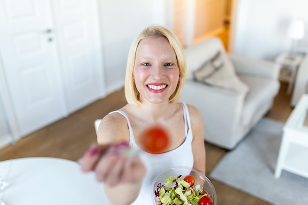 Portrait d'une jolie femme souriante caucasienne mangeant de la salade Jeune et heureuse femme mangeant une salade saine avec des ingrédients frais verts à l'intérieur