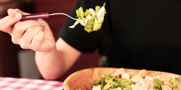 Portrait d'une jolie femme souriante caucasienne mangeant de la salade se concentrant sur la main et la fourchette