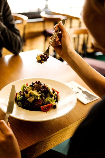 Portrait d'une jolie femme souriante caucasienne mangeant de la salade se concentrant sur la main et la fourchette