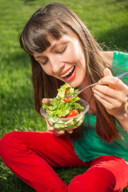 Portrait d'une jolie femme souriante caucasienne mangeant de la salade se concentrant sur la main et la fourchette