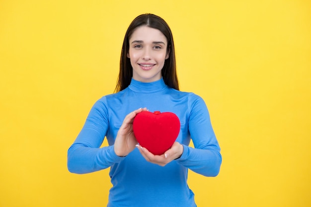 Portrait d'une jolie femme souriante tenant un coeur de papier dans ses mains sur fond jaune Concept d'amour