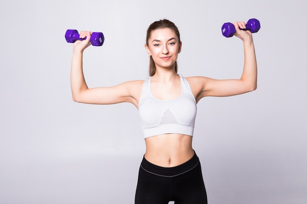 Portrait d'une jolie femme sportive tenant des poids isolés sur un mur blanc