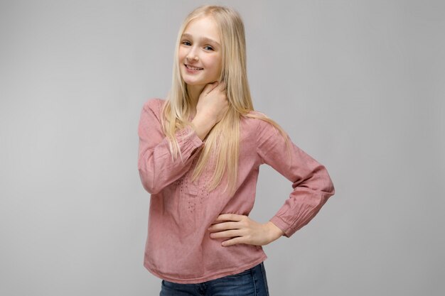 Portrait de jolie fille d&#39;adolescent blonde adorable attrayante en chemisier rose sur gris