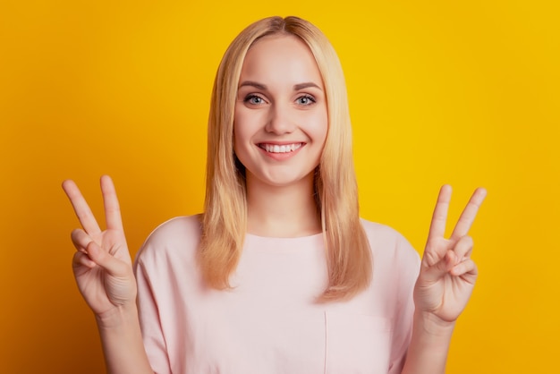 Portrait d'une jolie fille adorable souriante, les mains souriantes montrent un signe v sur fond jaune