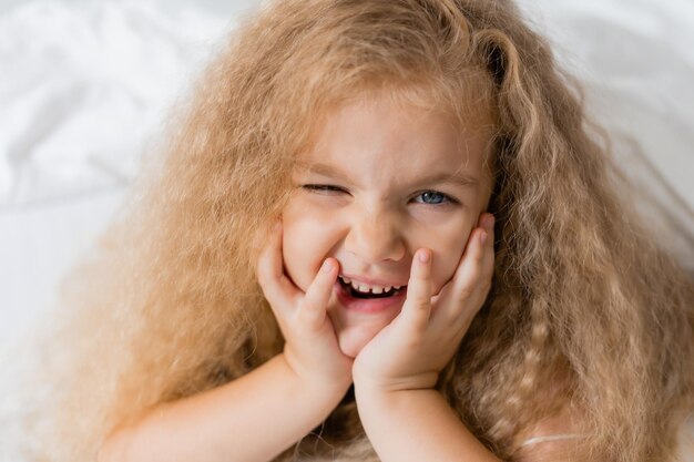 Portrait d'une jolie fille blonde bouclée souriante allongée dans le lit