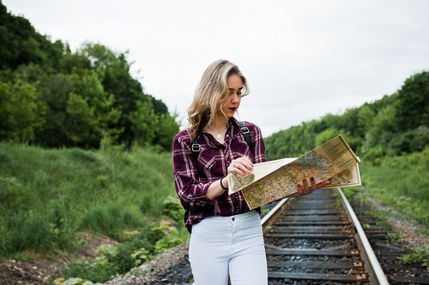 Portrait d'une jolie fille blonde en chemise de tartan marchant sur le chemin de fer avec la carte dans ses mains.