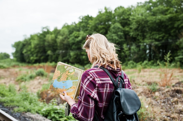 Portrait d'une jolie fille blonde en chemise de tartan marchant sur le chemin de fer avec la carte dans ses mains.