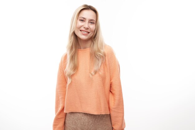 Portrait de jolie fille blonde en orange casual posant et souriant joyeusement isolé sur fond de studio blanc