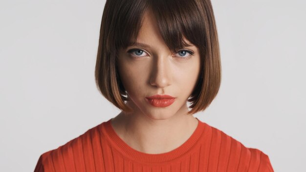Portrait d'une jolie fille brune aux cheveux bob et aux lèvres rouges a l'air sérieux devant la caméra isolée sur fond blanc