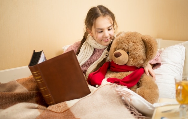 Portrait d'une jolie fille brune racontant une histoire à un ours en peluche au lit