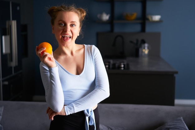 Portrait d'une jolie fille caucasienne faisant des grimaces tenant une orange juteuse fraîche entière à la maison dans