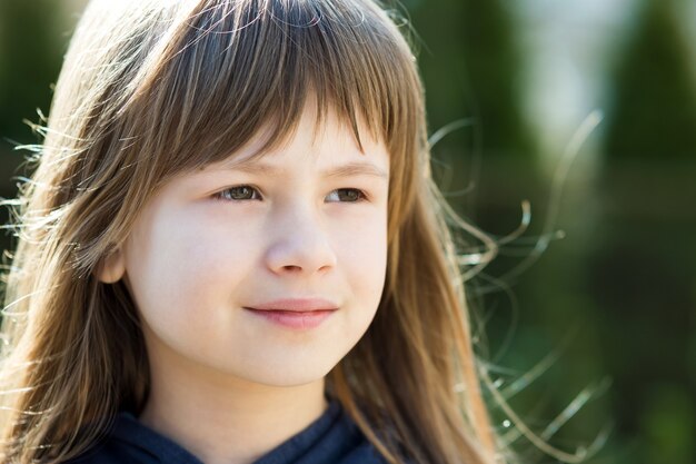 Portrait de jolie fille enfant aux yeux gris et longs cheveux blonds à l'extérieur sur fond clair flou.