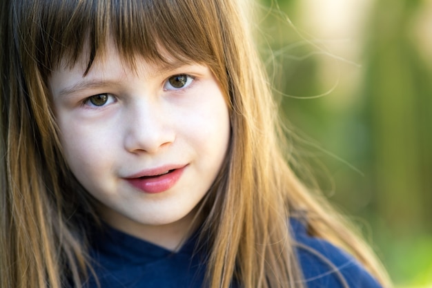 Portrait de jolie fille enfant aux yeux gris et de longs cheveux blonds à l'extérieur sur une surface lumineuse verte floue