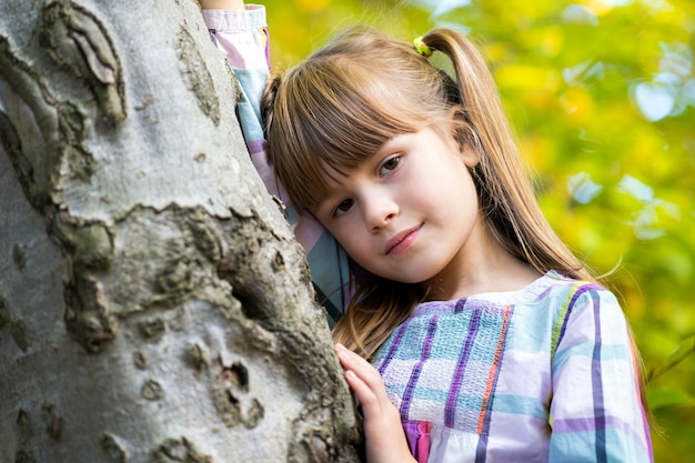 Portrait de jolie fille enfant s'appuyant sur un tronc d'arbre à l'automne parc relaxant