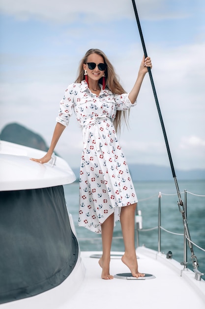 Portrait d'une jolie fille heureuse avec une robe blanche et de longs cheveux blonds bouclés debout sur un yacht en été. regardant la caméra avec un sourire à pleines dents.