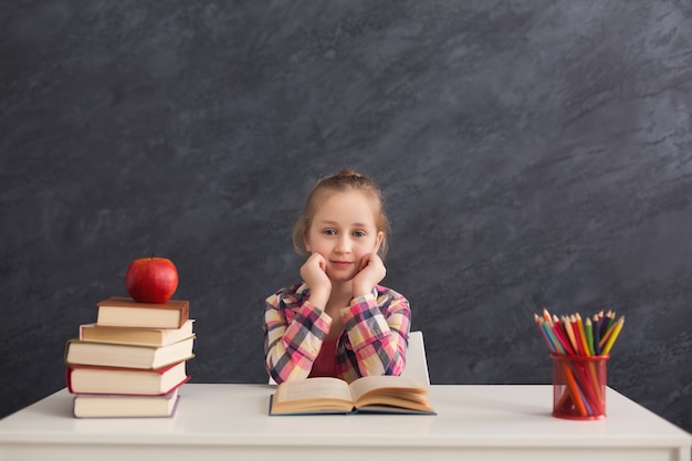 Portrait d'une jolie fille intelligente souriante assise avec une pile de livres à table, espace de copie. Concept d'éducation et de développement